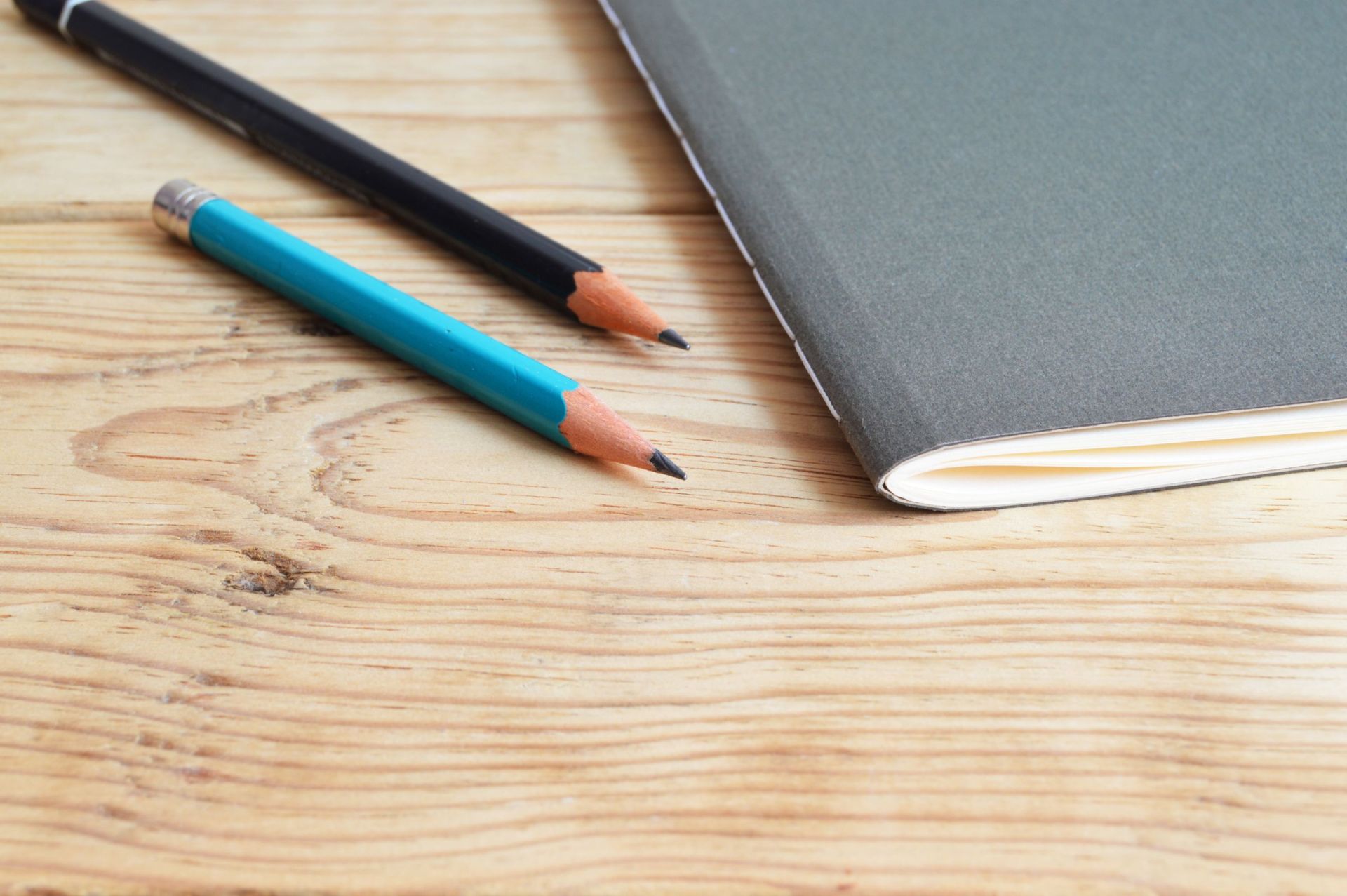 Two pencils beside a grey notebook on a wooden desk